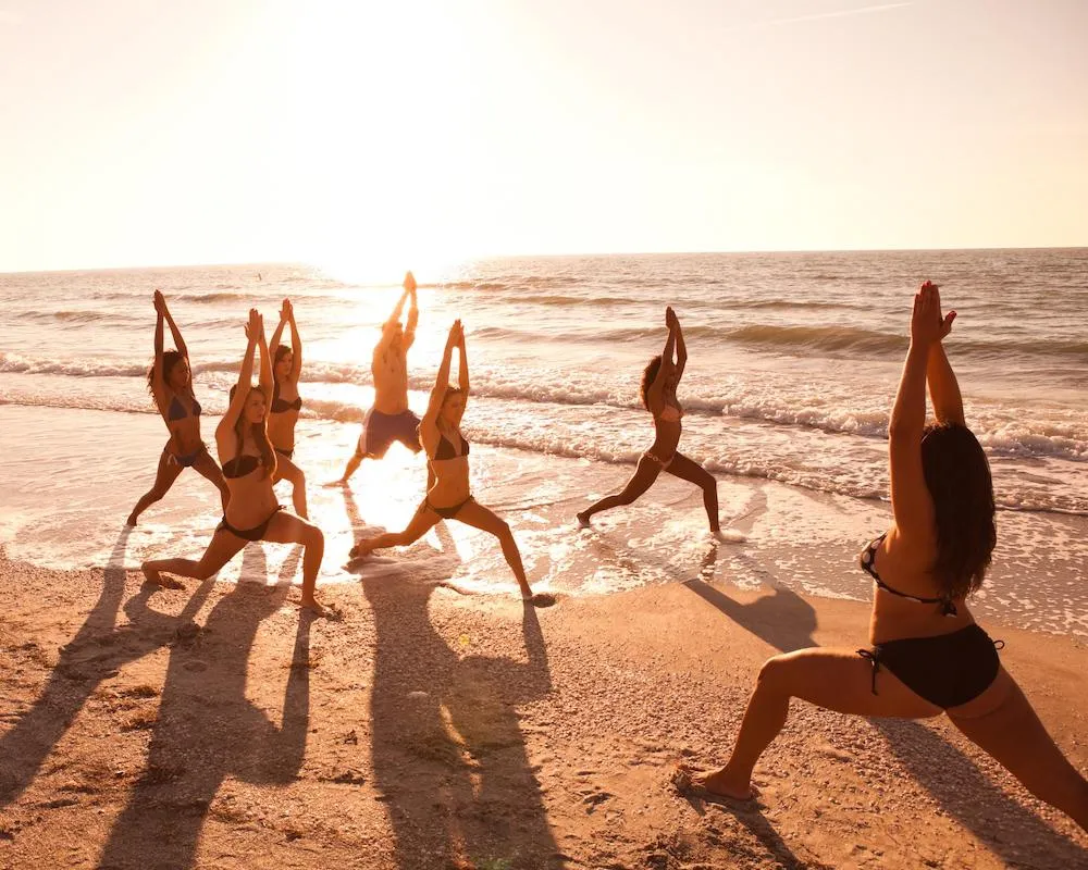 Group of yogis flowing through poses at sunrise by the shoreline.